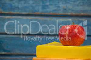 Stack of books and apple against blue wooden background