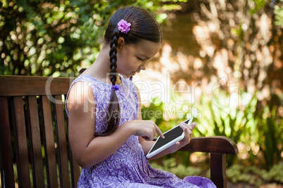 Girl using digital tablet while sitting on wooden bench