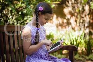 Girl using digital tablet while sitting on wooden bench