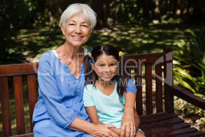 Portrait of senior woman with granddaughter sitting on wooden bench