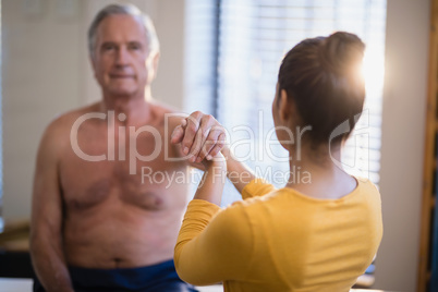 Rear view of female therapist giving arm massaging to senior male patient