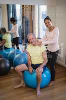 Portrait of smiling female therapist giving neck massage to senior patient sitting on exercise ball