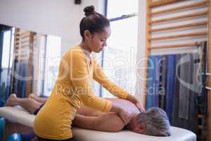 Young female therapist giving neck massage to senior male patient lying on bed