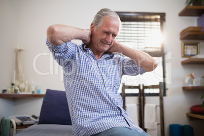 Low angle view of senior male patient sitting with neck pain on bed