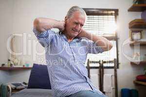 Low angle view of senior male patient sitting with neck pain on bed