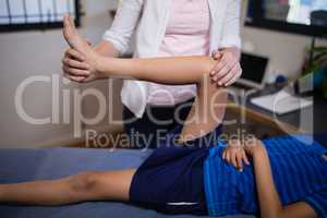 Midsection of female therapist massaging knee with boy lying on bed