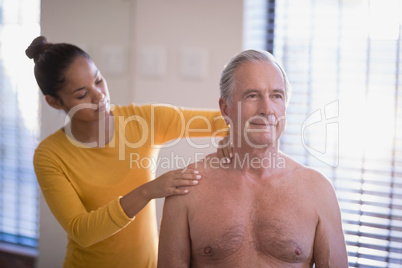 Female therapist giving neck massage to shirtless senior male patient