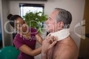 Female therapist examining neck collar on senior male patient