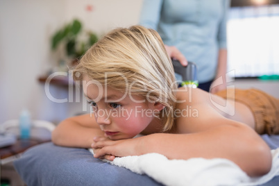 Close-up of boy lying on bed while female therapist using ultrasound machine