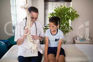 Smiling young female therapist explaining boy with artificial spine