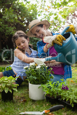 Happy mother with daughter watering potted plants in backyard