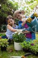 Happy mother with daughter watering potted plants in backyard
