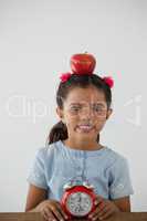 Schoolgirl sitting with apple on her head and alarm clock