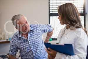 Senior male patient showing back ache to female doctor with file