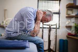 Side view of senior man sitting with neck pain on bed