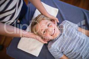 High angle portrait of smiling smiling boy receiving massage from female physiotherapist