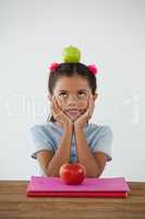 Schoolgirl sitting with green apple on her head against white background