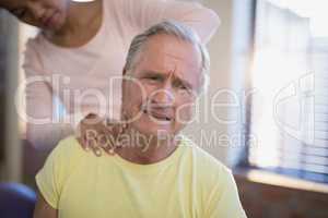 Senior male patient frowning while receiving neck massage from therapist