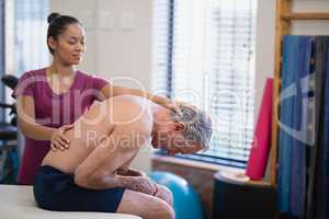 Young female therapist giving back massage to senior male patient bending on bed