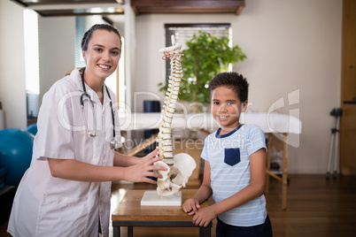 Portrait of smiling boy and female therapist standing with artificial spine on table