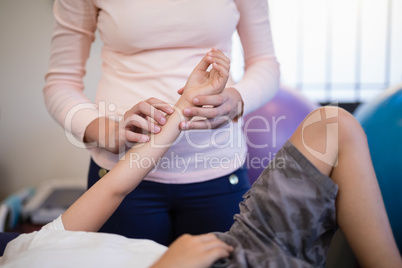 Midsection of female therapist tracing pulse while boy lying in examination room