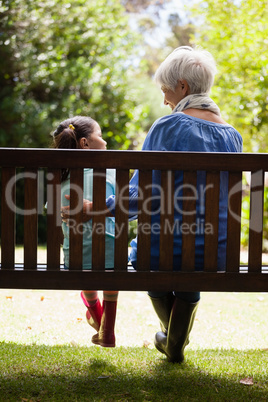 Rear view of grandmother and granddaughter sitting on wooden bench