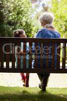 Rear view of grandmother and granddaughter sitting on wooden bench