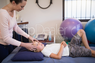 Young female therapist giving head massage to boy lying on bed