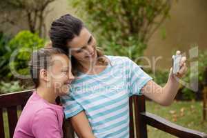 Smiling mother taking selfie with daughter sitting on bench