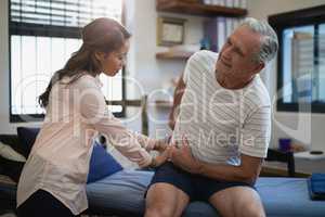 Senior male patient sitting on bed while female therapist examining back
