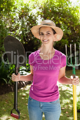 Portrait of smiling beautiful woman holding shovel and gardening fork