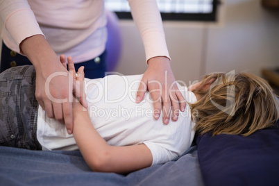 Female therapist examining arm of boy lying on bed