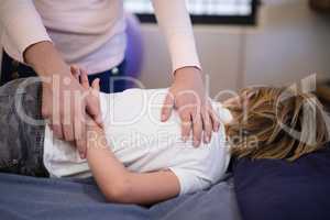 Female therapist examining arm of boy lying on bed