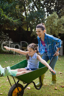 Happy woman pushing daughter sitting in wheelbarrow