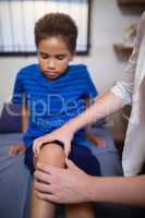 Boy looking while female therapist massaging knee