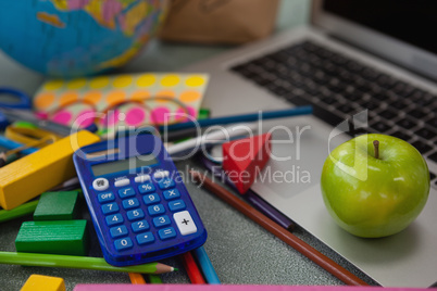 Various school supplies, apple and laptop on chalkboard
