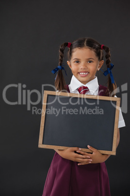 Portrait of schoolgirl holding blank slate against blackboard