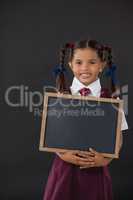 Portrait of schoolgirl holding blank slate against blackboard