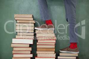 Schoolboy climbing steps of books stack against chalkboard