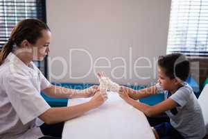 Side view of female therapist wrapping bandage on hand while boy sitting at table