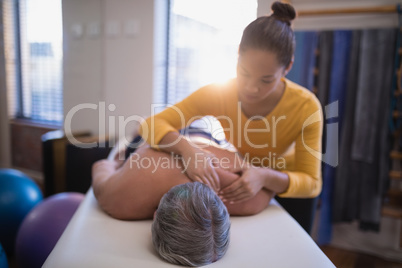 Shirtless male patient lying on bed receiving neck massage from female therapist