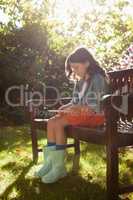 Full length of girl using phone while sitting on wooden bench