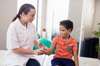 Young female therapist examining hand of boy while sitting on bed