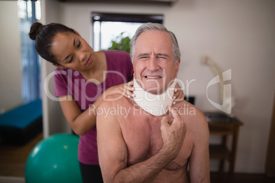 Female therapist looking at senior male patient grimacing with neck collar