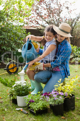 Happy mother teaching daughter to water plants