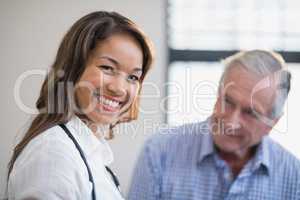 Portrait of smiling female therapist with senior male patient in background
