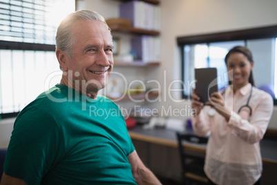 Portrait of smiling senior male patient with female therapist holding digital tablet