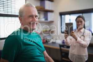 Portrait of smiling senior male patient with female therapist holding digital tablet