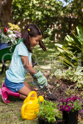Side view of girl kneeling while digging soil with trowel