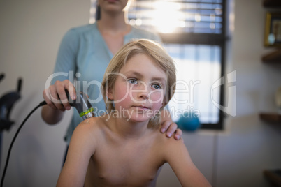 Blond boy sitting while female therapist using ultrasound machine